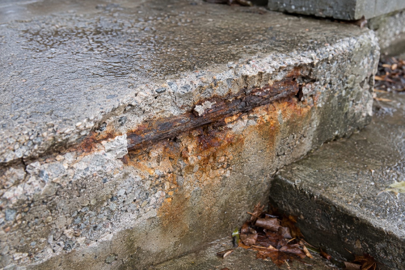 Spalled concrete edge with rusted rebar exposed and rust staining the concrete